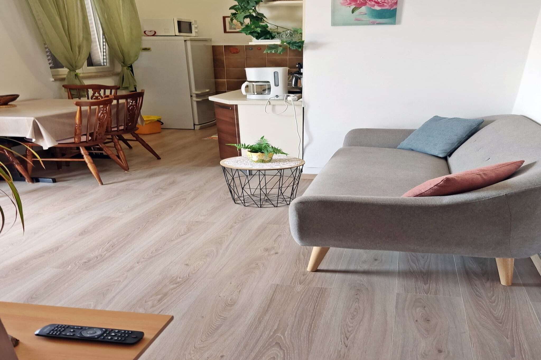 Ein Wohnzimmer mit grauem Sofa, einem kleinen runden Couchtisch und einem Essbereich mit Holztisch und Stühlen.