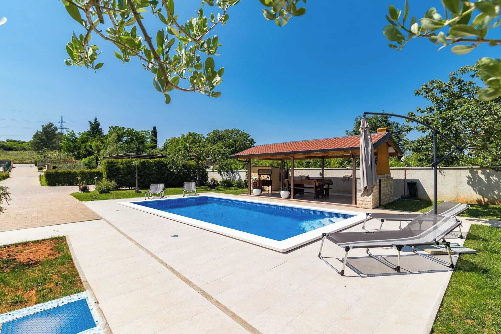 A swimming pool with lounge chairs, a covered patio, and a view of the surrounding greenery.