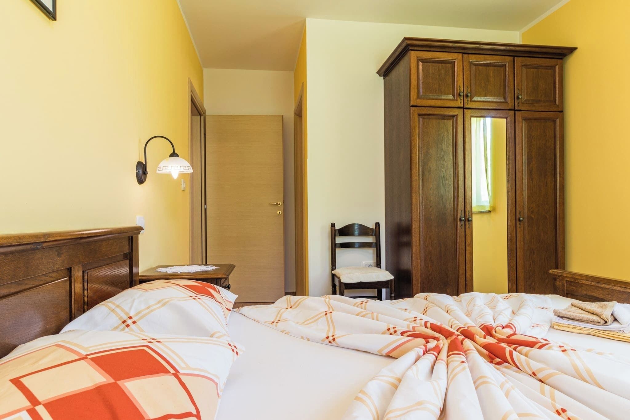 A hotel room with a bed, a wooden wardrobe, a chair, and a nightstand.
