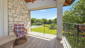 A balcony with a wicker chair, stone wall, and a view of a swimming pool and green landscape. - Charming Villa with Pool (Nedešcina)
