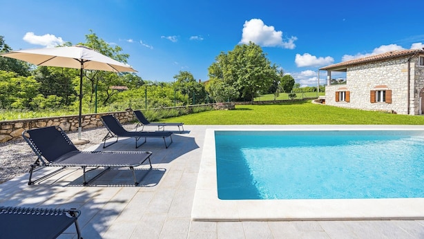 A swimming pool with lounge chairs and umbrellas, surrounded by a stone house and lush greenery. - Charming Villa with Pool (Nedešcina)