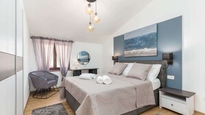 Un dormitorio moderno con una cama grande, mesitas de noche, una silla, un espejo y un cuadro en la pared.