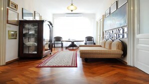 A hallway with a wooden floor, a red and white rug, a sofa, a cabinet with glass doors, and framed pictures on the walls.