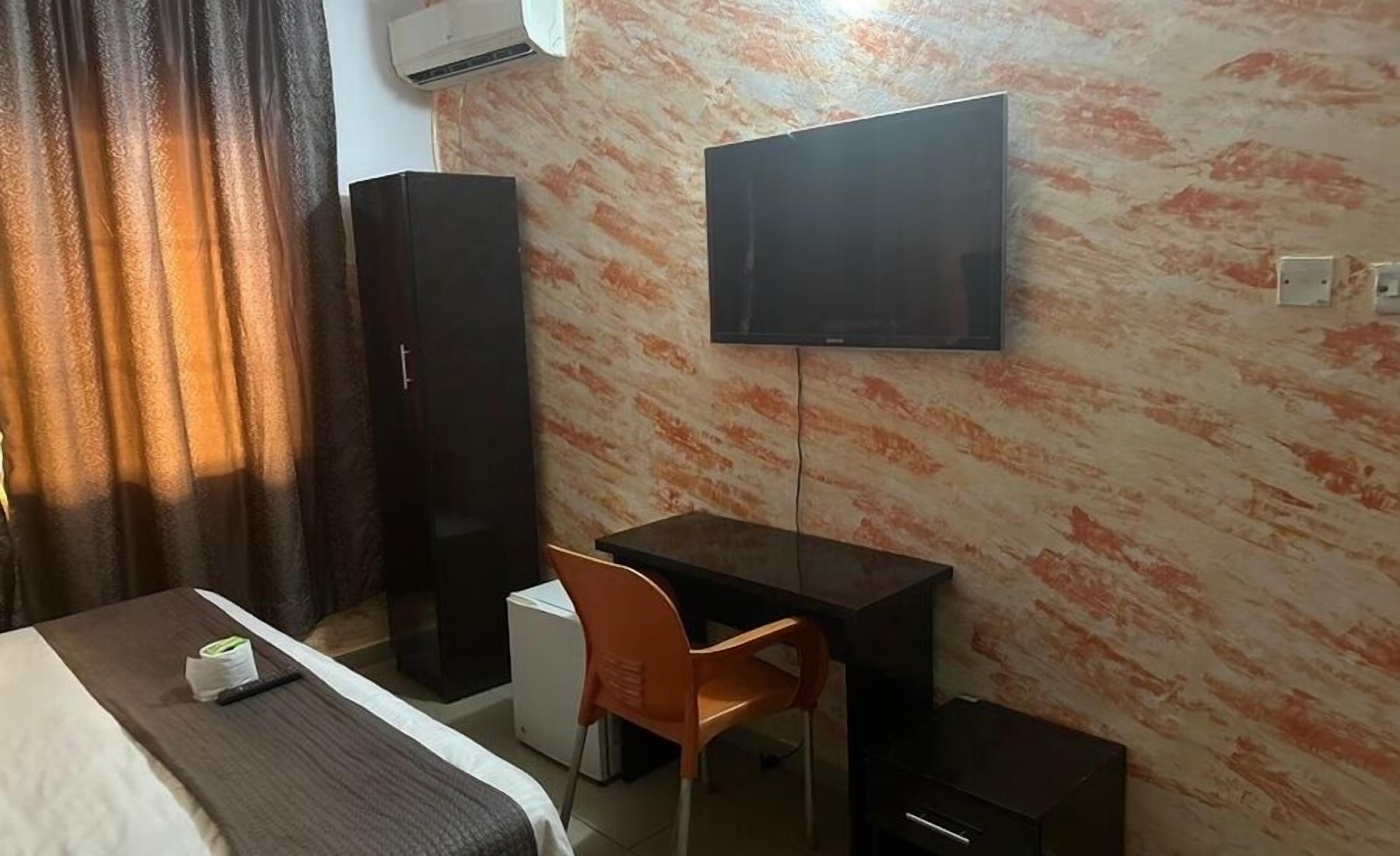 Una habitación de hotel con cama, escritorio, silla, televisor y armario.