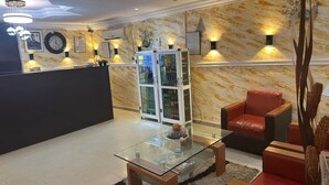 Een receptiegedeelte met een tafel met glazen blad, een rode leren bank en een receptiebalie met een klok en ingelijste certificaten.