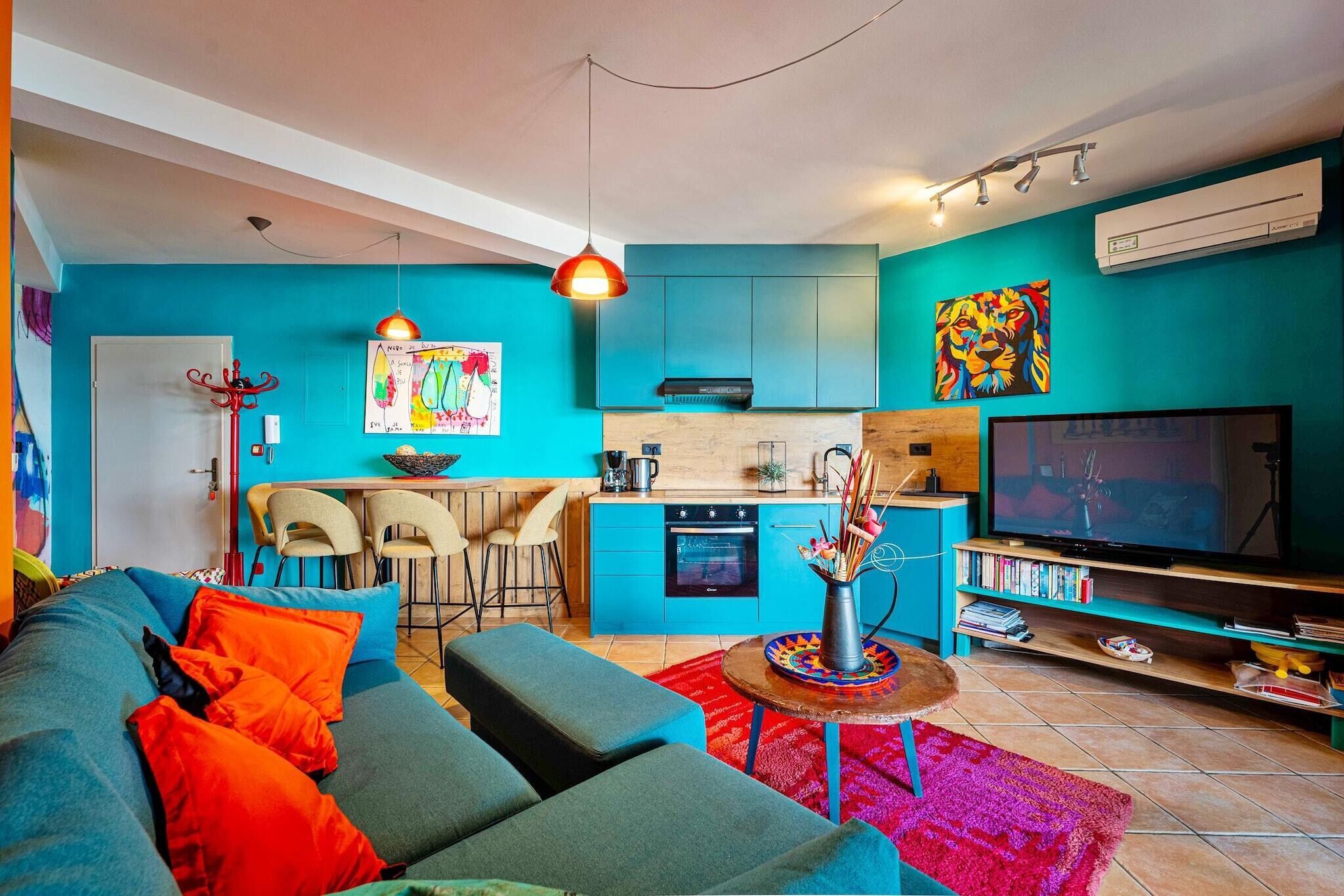 A modern living room with a sofa, a coffee table, and a TV. There is a kitchen area with a stove, oven, and sink.