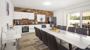 A modern kitchen with white cabinets, a stone backsplash, and a dining area with a white table and dark chairs. - Luxe villa in Pula with pool and jacuzzi (Pula)