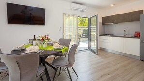 A modern dining area with a table set for four, a kitchen with integrated appliances, and a sliding glass door leading to an outdoor area.