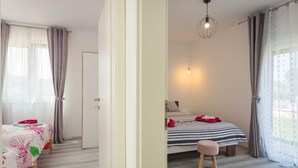 A bedroom with two beds, a wooden floor, a white door, and a hanging light fixture.