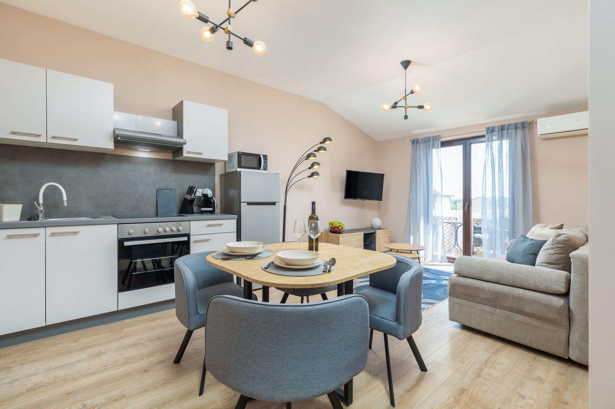 Una cocina moderna con armarios blancos, una mesa de comedor con cuatro sillas, un televisor y un sofá en la sala.