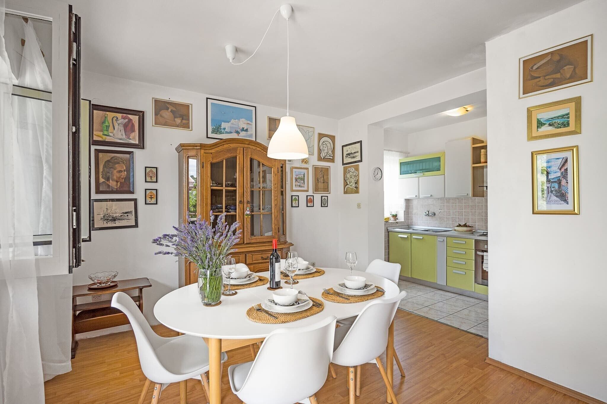 A dining area with a round table set for four, white chairs, a wooden cabinet, and various framed pictures on the walls.
