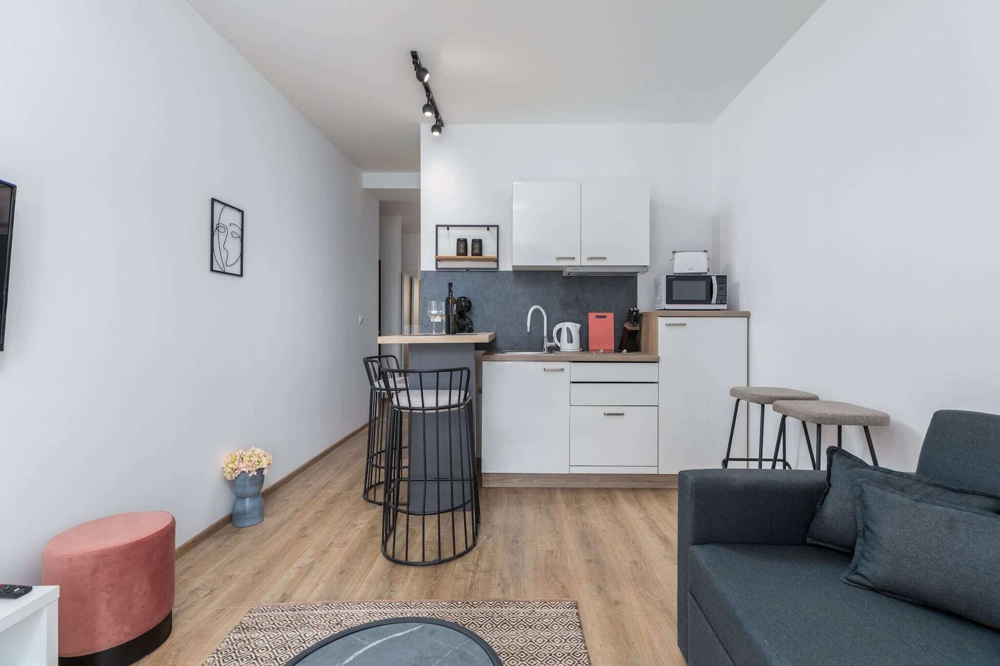 A compact living space with a kitchenette, a dining area with a small table and chairs, a sofa, and a red accent chair.