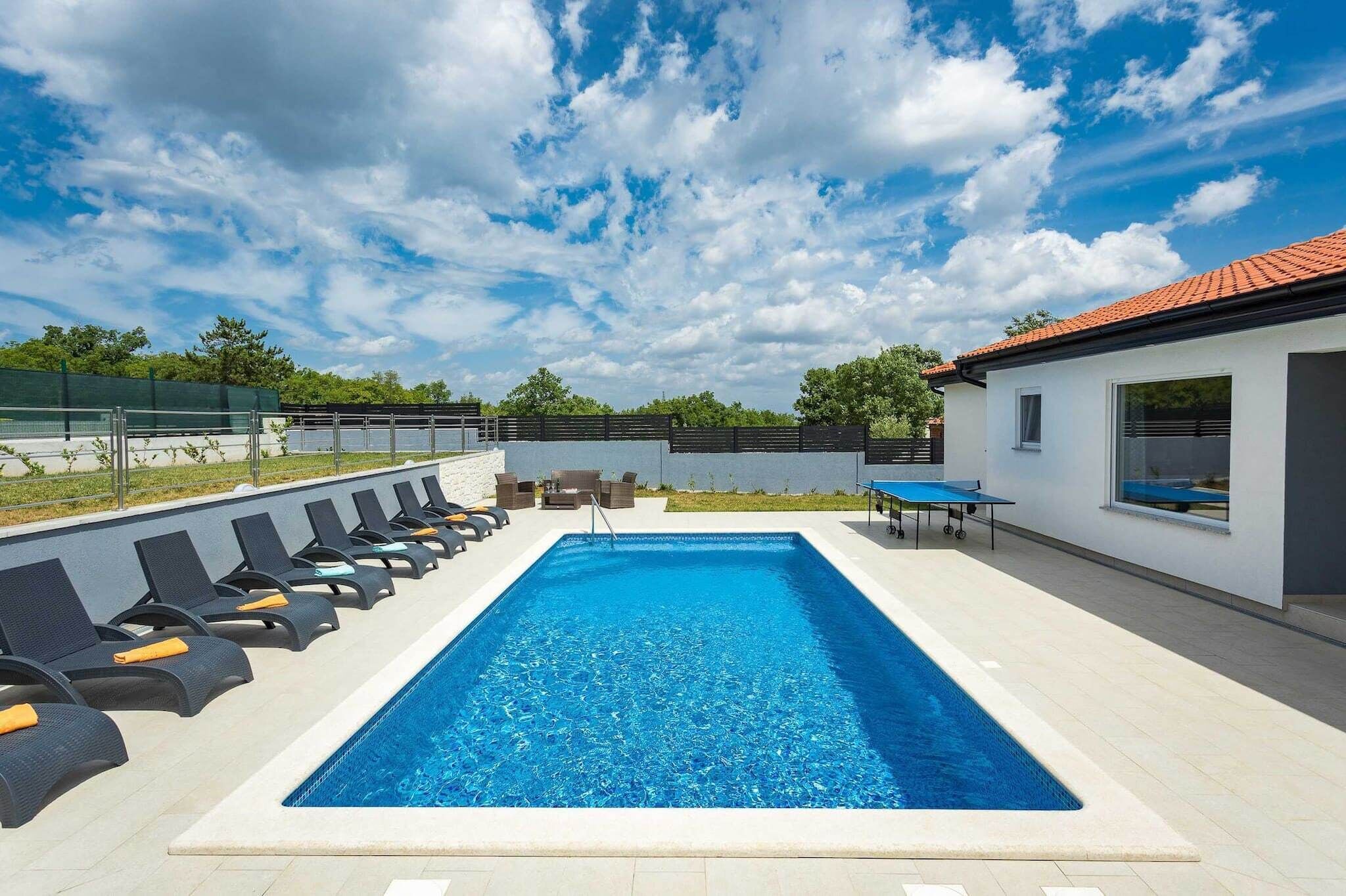 Una piscina rettangolare con lettini e un tavolo, circondata da un edificio bianco con tetto in tegole.