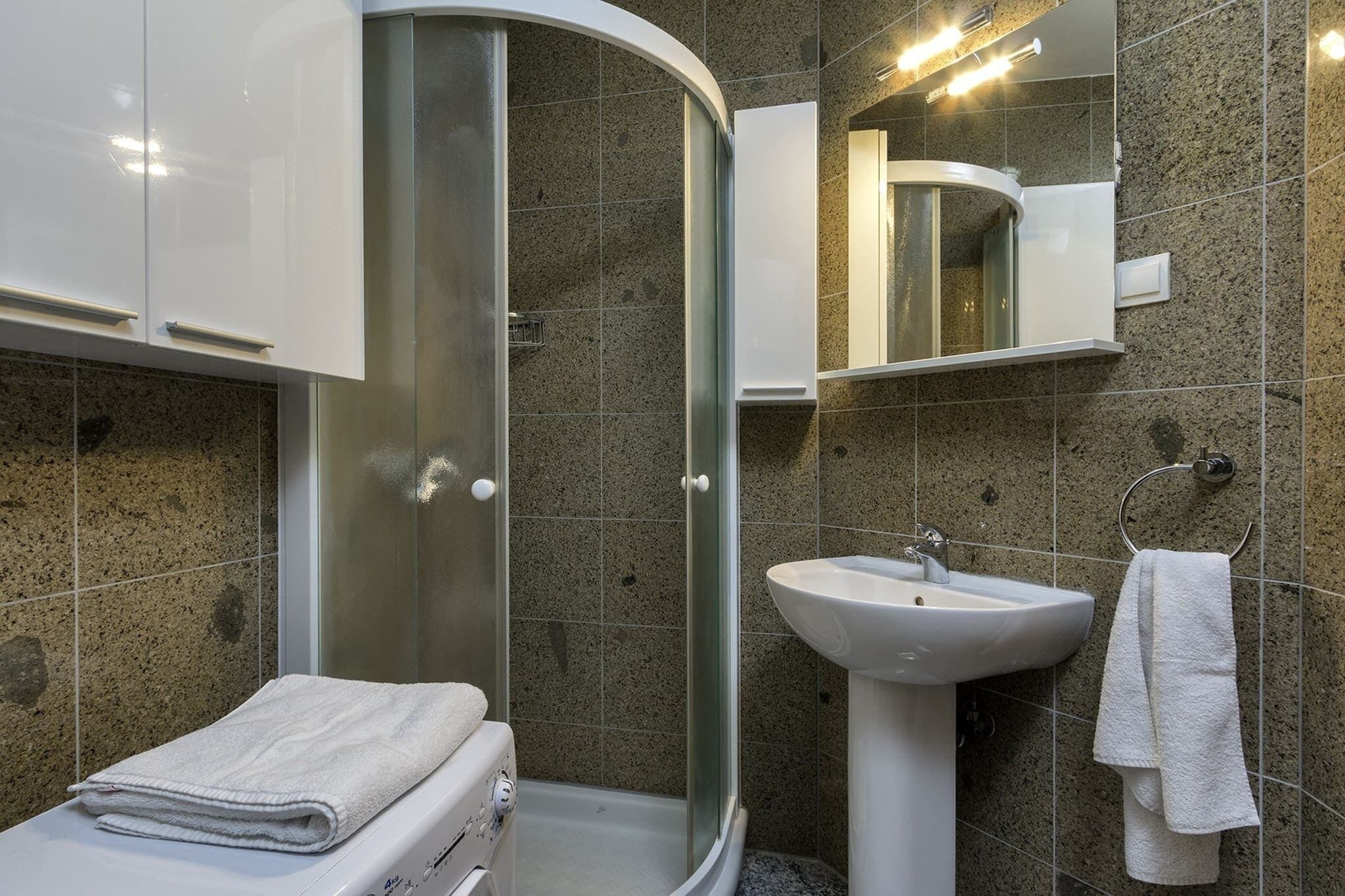 Une salle de bain moderne avec une douche en verre, un lavabo blanc et une serviette sur le sol.