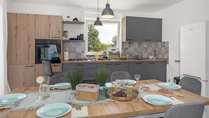 A modern kitchen with wooden cabinets, a built-in oven, and a dining area set for a meal. - Modern Rscape with Pool (Baderna)