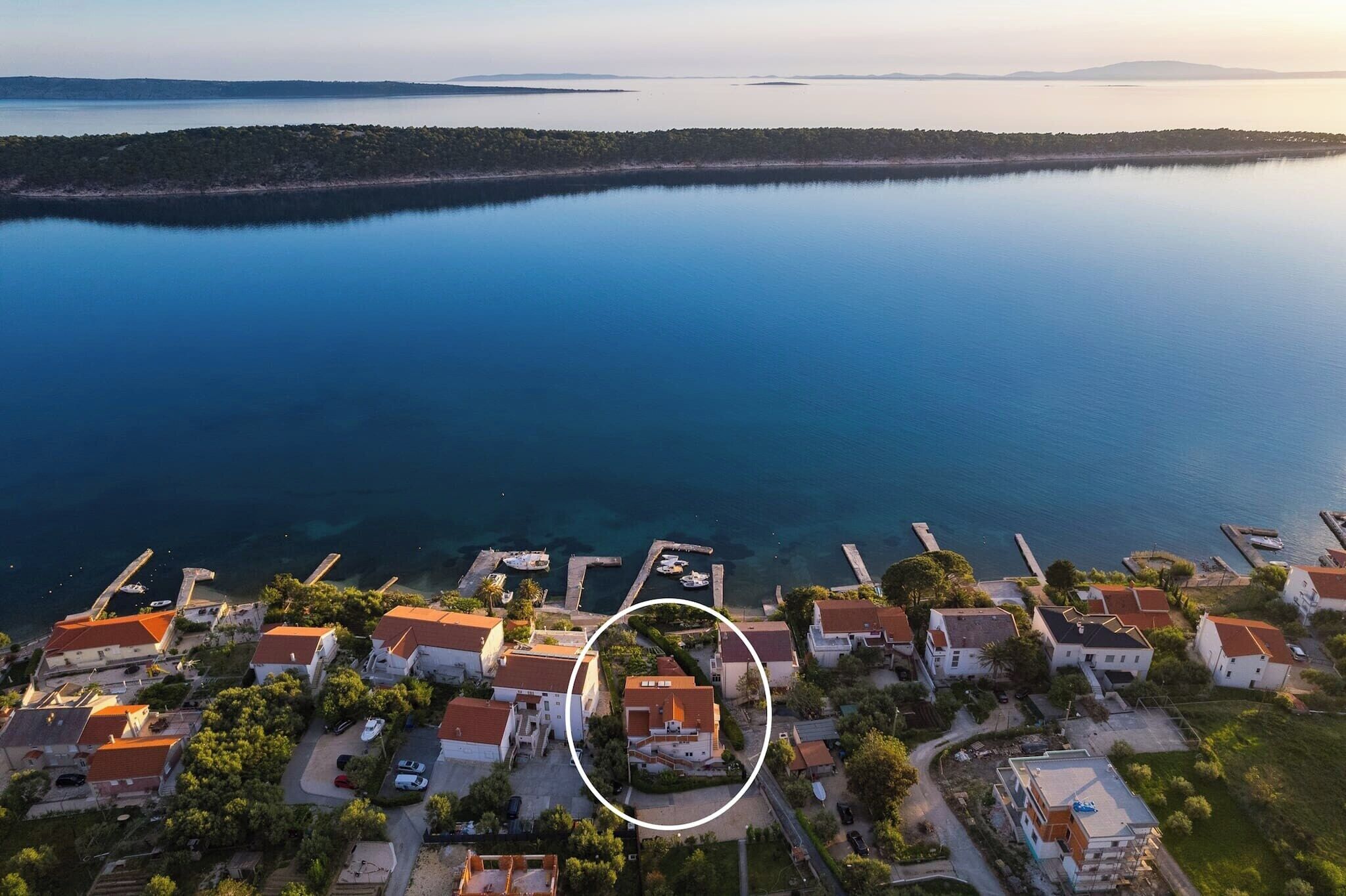 An aerial view of a coastal village with houses, a marina, and a calm sea.