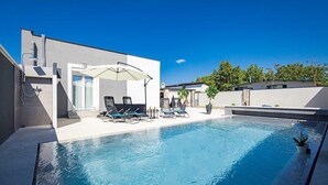 A modern pool area with a clear blue pool, lounge chairs, and a covered seating area.