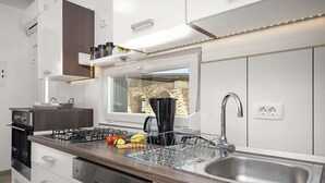A modern kitchen with a built-in stove, a large sink, and a window overlooking a stone wall.