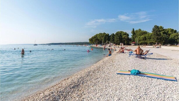 A pebbled beach with people sunbathing and swimming.