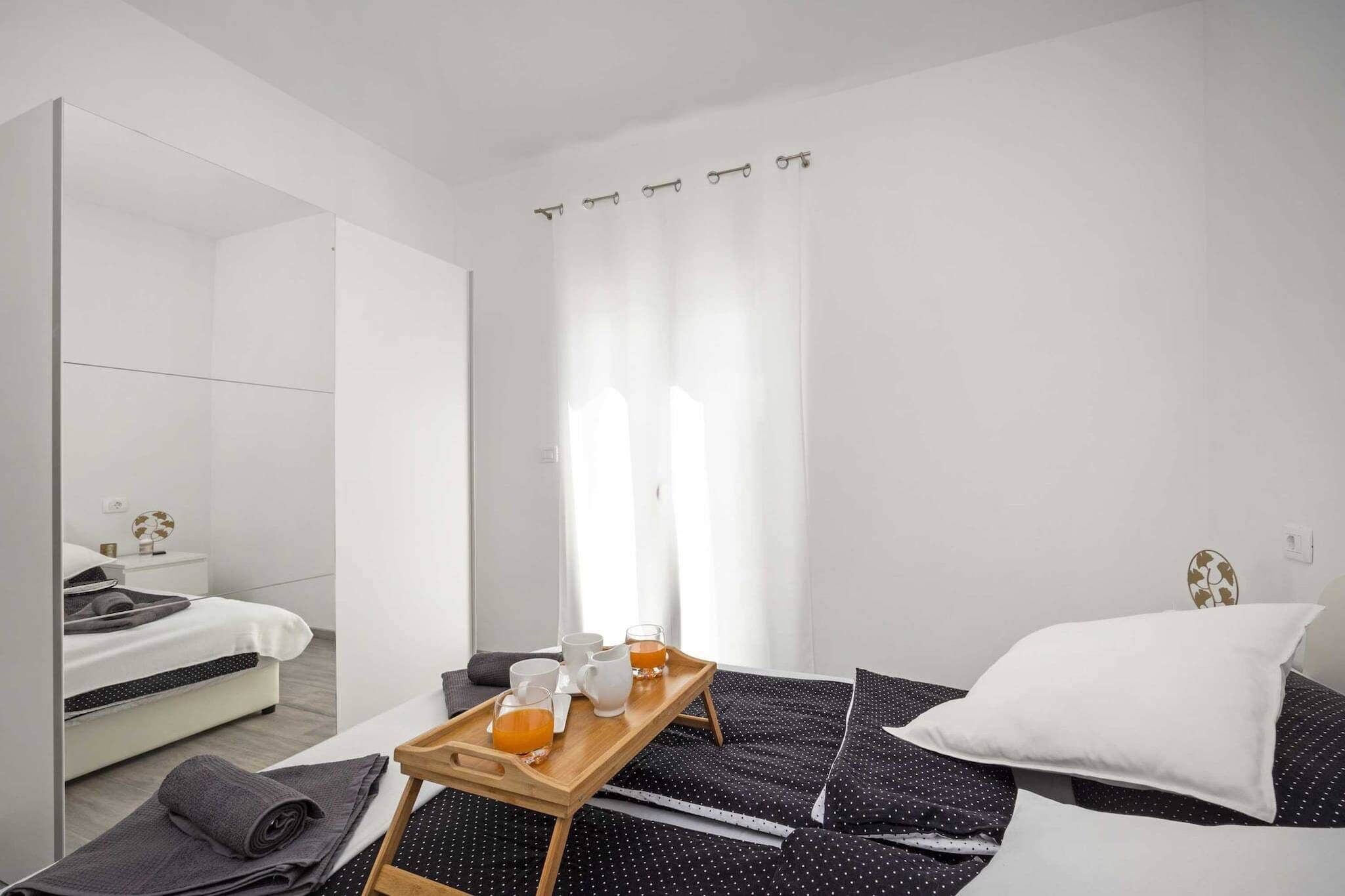 Ein modernes Hotelzimmer mit einem Bett, einer Holzwanne mit Getränken, einem Spiegel und einem Fenster mit Vorhängen.