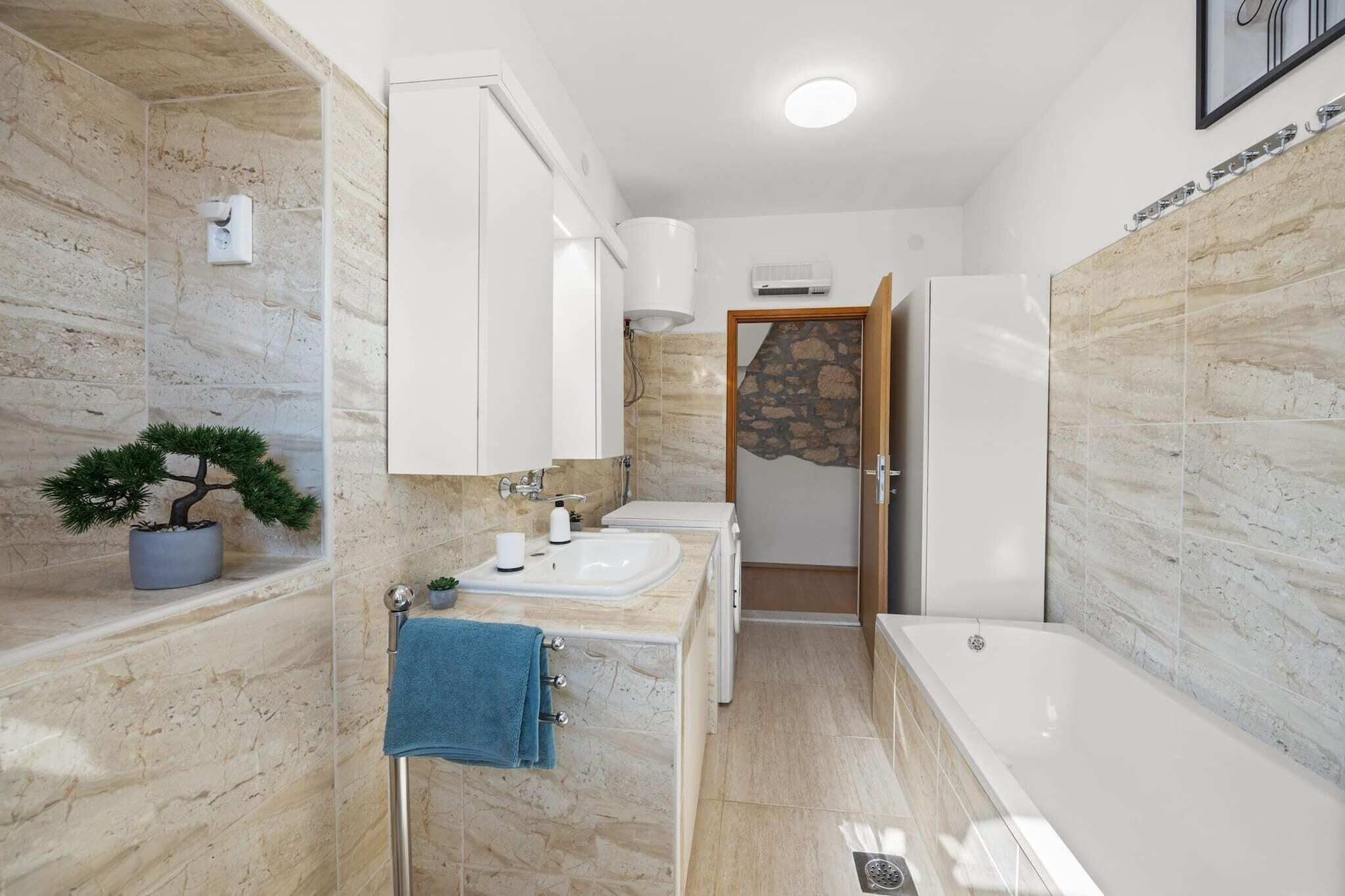 Un baño moderno con pared de mármol, lavabo, bañera y planta en maceta.