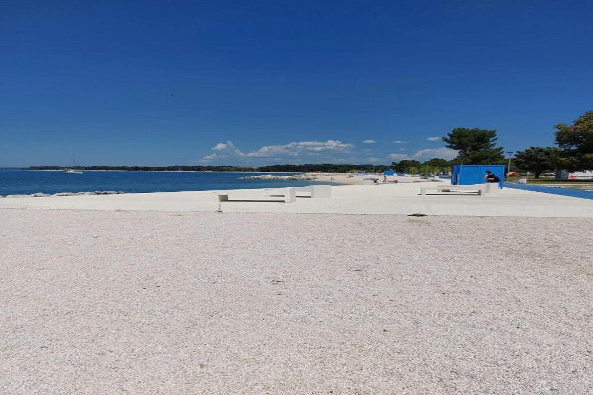 Una playa con un paseo marítimo de concreto, una estructura azul y un cielo despejado.