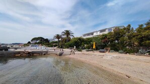 Una zona costera con un cuerpo de agua cristalina, una playa de arena y un edificio con balcón que da al agua.