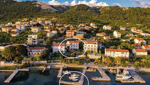 Vista aérea de un pueblo costero con edificios, un puerto deportivo y montañas al fondo.