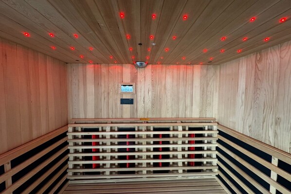 A sauna with wooden walls and ceiling, a bench, and red lighting.