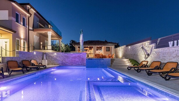 Una piscina con sillas de descanso, un muro de piedra y un edificio con balcón.