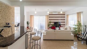 Una sala de estar moderna con un sofá, una mesa de centro y un televisor. Hay dos ventanas con cortinas, una pared de ladrillo y una lámpara en el techo.