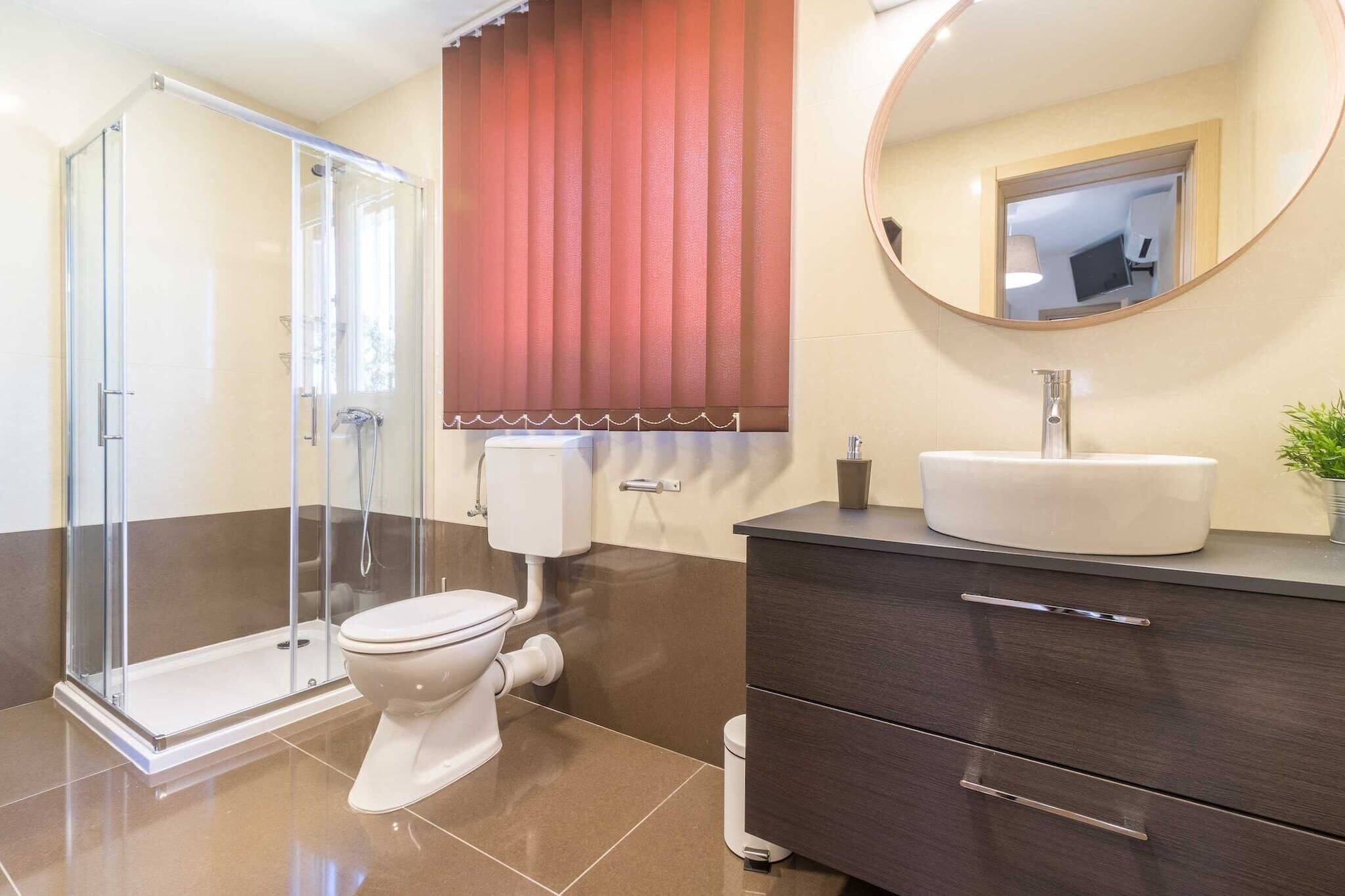 A modern bathroom with a glass shower enclosure, a toilet, a vanity with a sink, and a mirror.