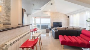 Una sala de estar moderna con un sofá rojo, un mueble seccional negro y una cocina con salpicadero de piedra y taburetes de bar rojos.