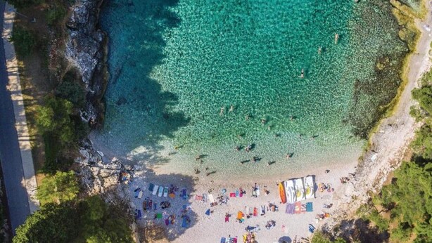 An aerial view of a beach with clear turquoise water, a sandy shore, and several colorful umbrellas and beach chairs. - House in Fažana near Rock Beach (Fažana)