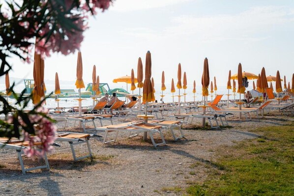A beach with rows of sun loungers and umbrellas, some occupied, others empty.