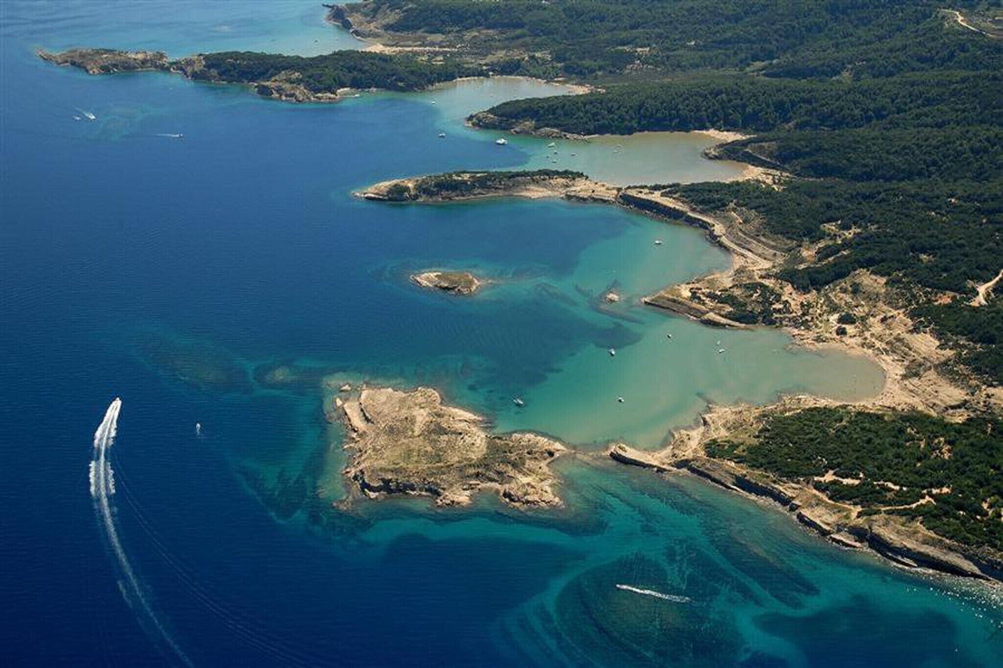 Une vue aérienne d’une zone côtière, avec des eaux bleues et limpides, des plages de sable et une végétation verdoyante.