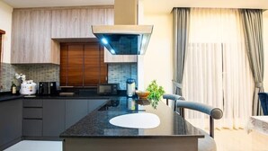 A modern kitchen with dark cabinetry, a central island, and a built-in stove. - Level Flow pool villa Pattaya (Sattahip)
