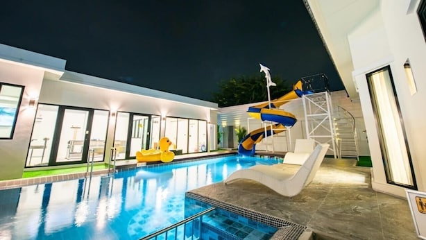 An indoor swimming pool with a water slide, lounge chairs, and a modern building with large windows. - Level Flow pool villa Pattaya (Sattahip)