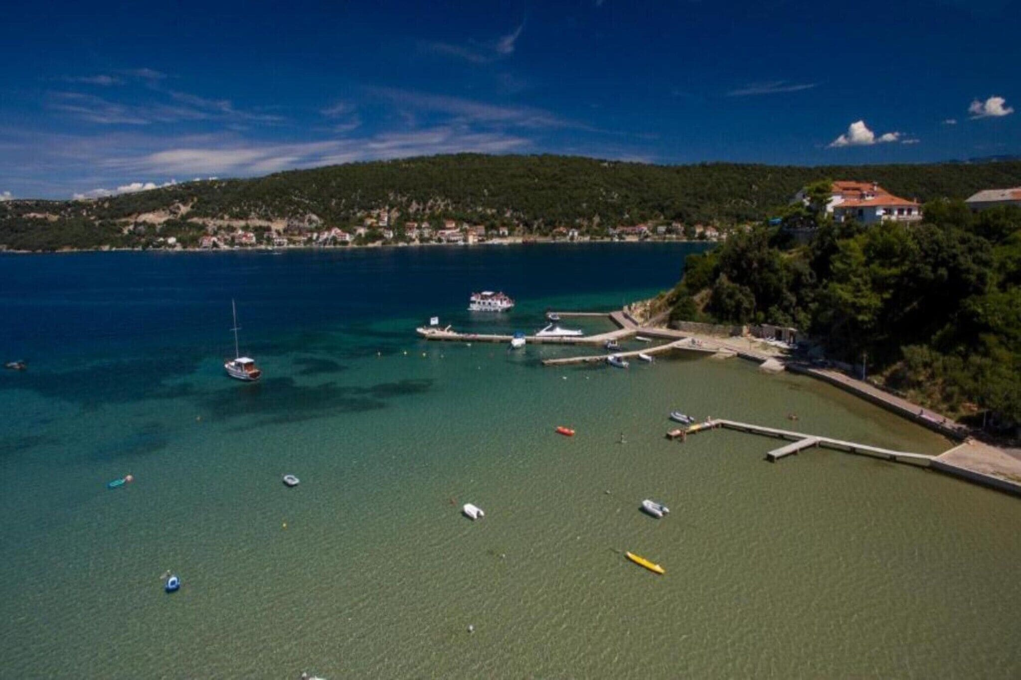 A coastal area with boats docked at a pier, a clear blue sky, and a hill with buildings in the background.