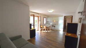 A living room with a sofa, a dining area with a table and chairs, a kitchen with cabinets and appliances, and a hallway leading to another room.
