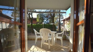 A glass door leading to an outdoor patio with a table and chairs, a hammock, and a view of trees and buildings.