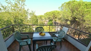 Un balcon avec une table et des chaises, un panier de fruits et une vue sur les arbres.
