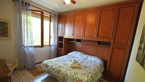 Une chambre à coucher avec un lit, des armoires en bois, une fenêtre avec des rideaux et un ventilateur de plafond.