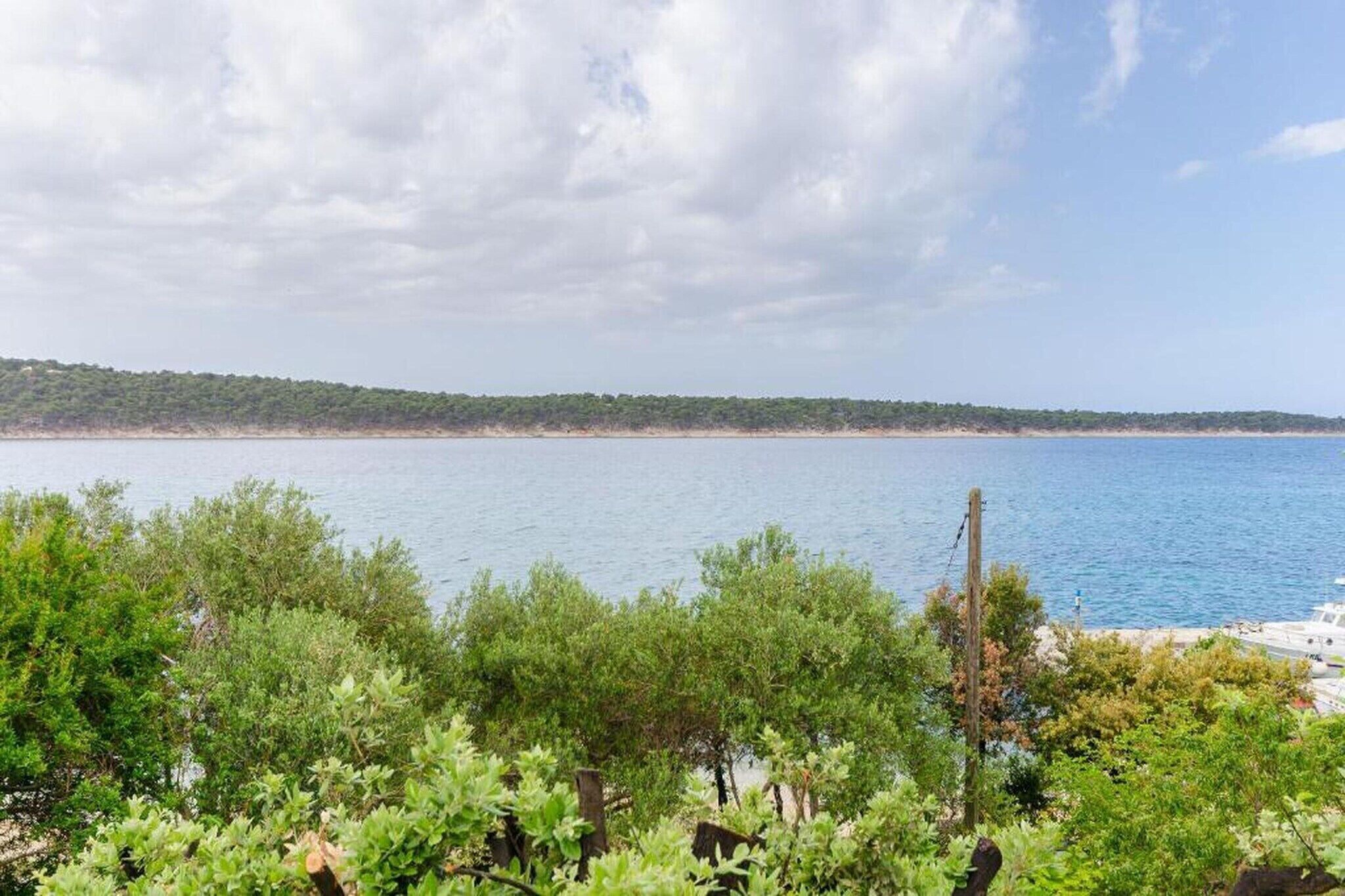 A coastal landscape with a clear view of the sea and a distant tree-covered shoreline.