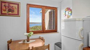 A small kitchen with a wooden table, a refrigerator, and a window with a view. - Apartment in Supetarska Draga near Sandy Beach (Supetarska Draga)