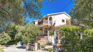 A two-story building with a balcony, surrounded by trees and a stone wall. - Apartment in Supetarska Draga near Sandy Beach (Supetarska Draga)