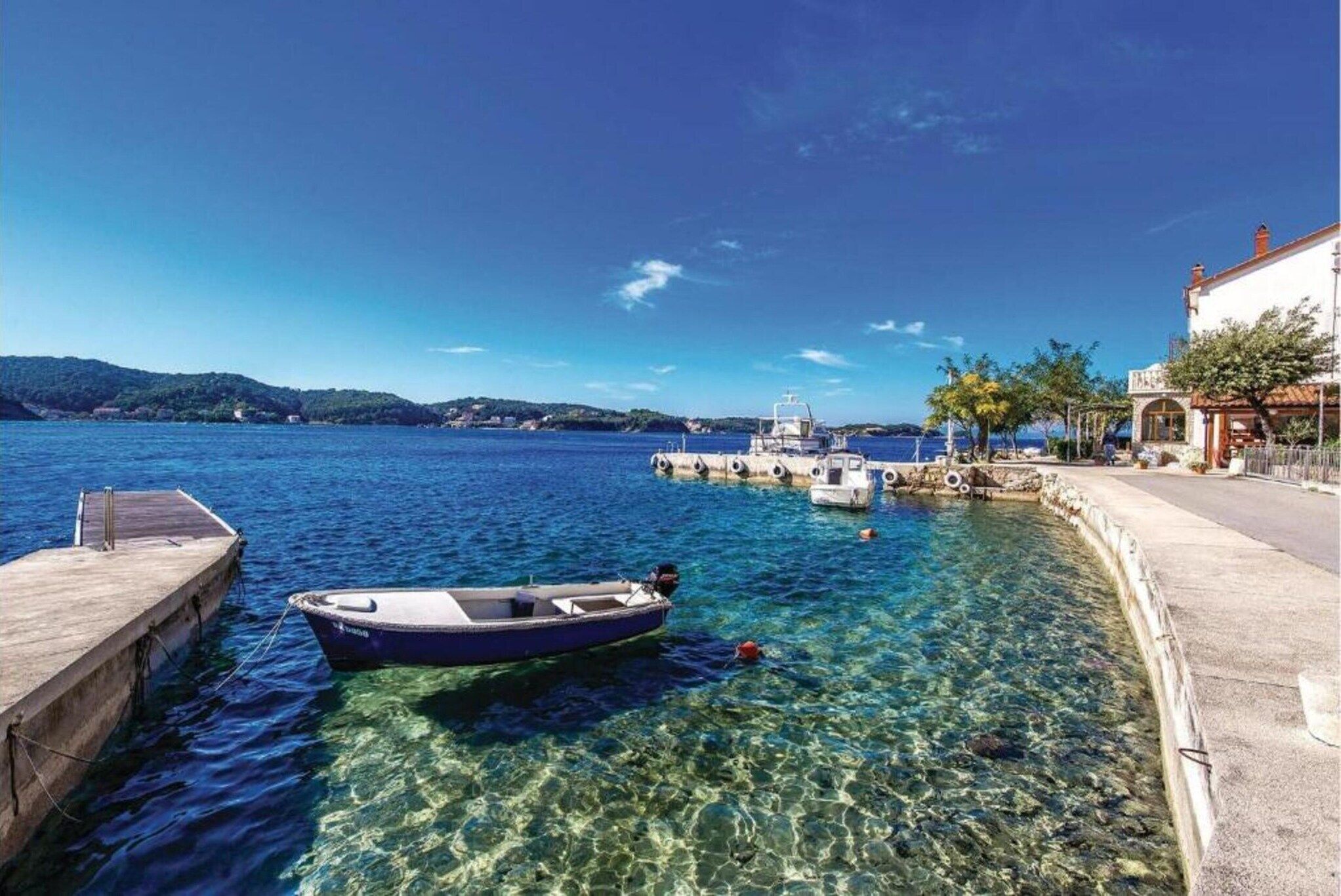 A coastal scene with a clear blue sea, a dock, a small boat, and a building with a sign.