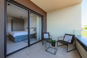 A modern bedroom with a bed, a sliding glass door leading to a balcony, and a small table with a plant.