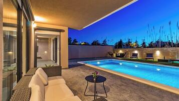 A modern outdoor pool area with a clear blue pool, lounge chairs, and a sofa.