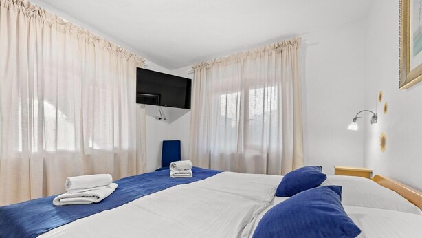 A hotel room with two beds, a flat-screen TV mounted on the wall, and a bedside table with a lamp. - Villa Pineta two bedroom apartment (Medulin)